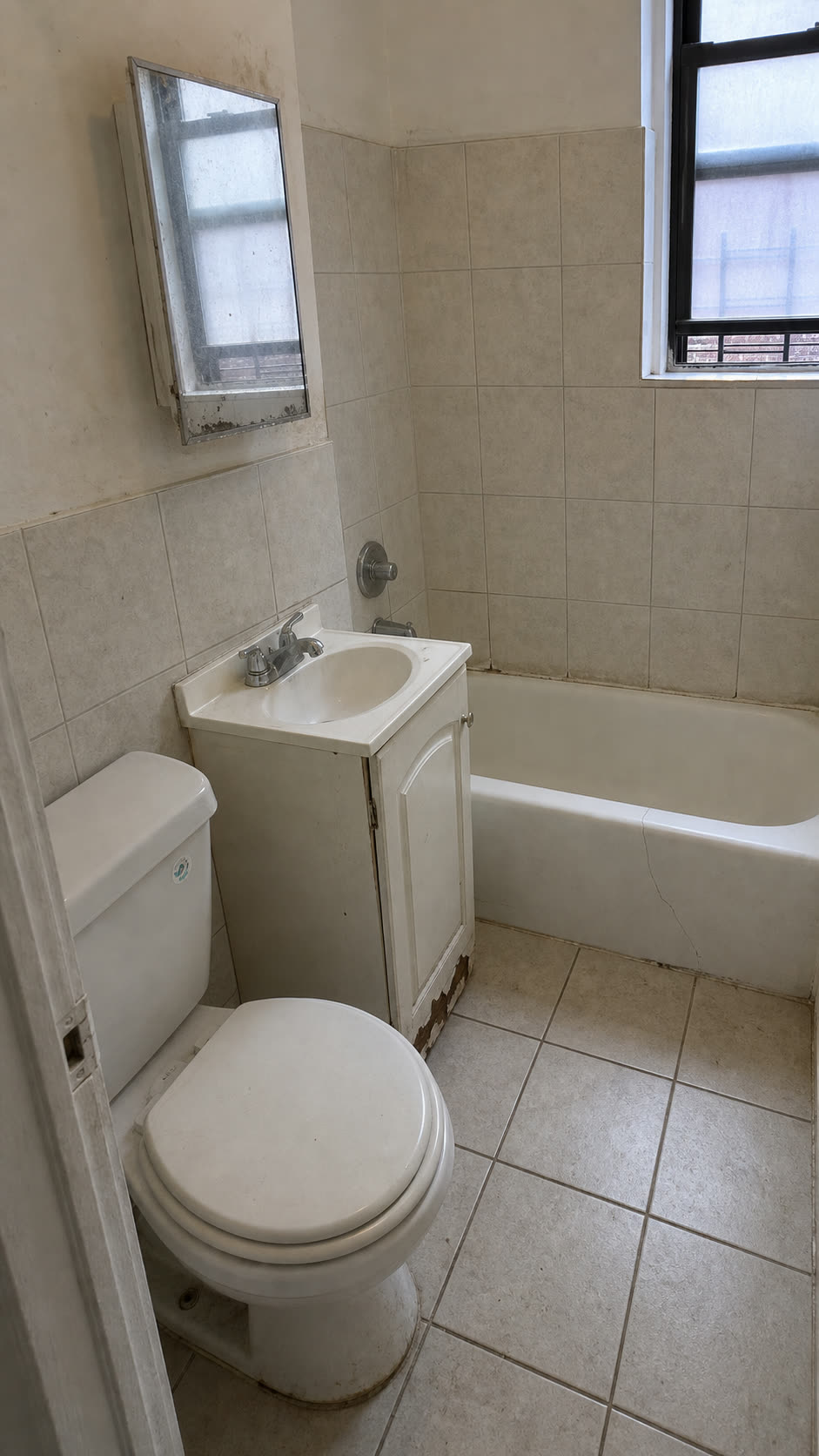 Bathroom before renovation — worn tile, damaged vanity, cracked tub